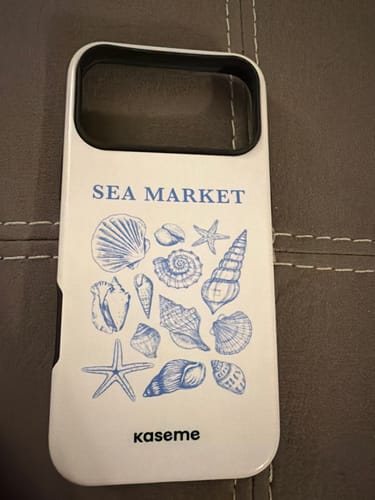 Reviewer's white Souvenir phone case with a blue seashell and starfish design on a textured surface.