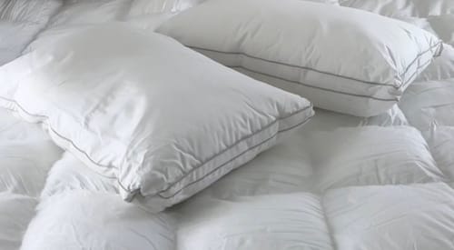 Reviewer's two white Hotel Cloud Collection™ pillows with grey piping, lying on a bed.