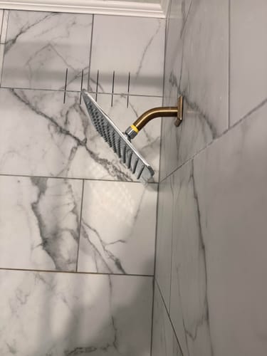 Reviewer's installed 8 Inch Square Rain Shower Head on a brass arm against white marble-patterned tile.
