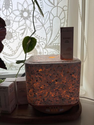 Recensent toont het doosje Bergamot etherische olie bovenop een sfeervol verlichte aroma diffuser.