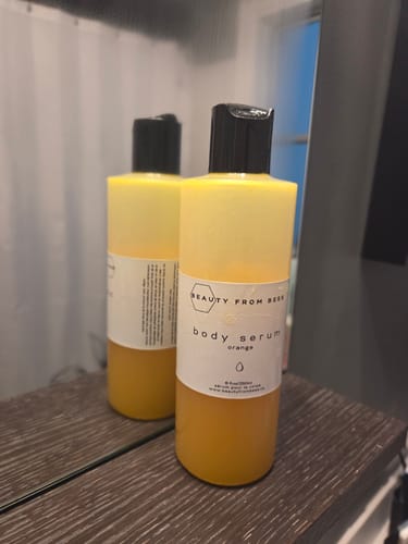 Customer's two-toned Orange Body Serum bottle on a dark wood counter, reflected in a mirror.