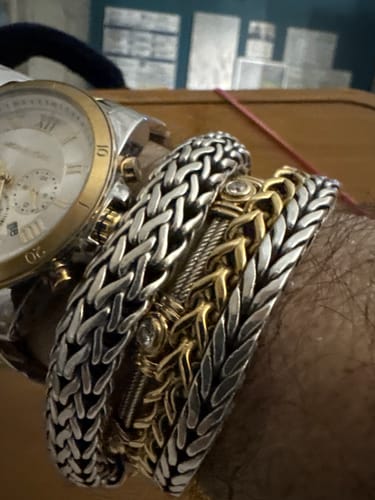 Close-up of a customer's wrist wearing the gold-tone Cuban Link Bracelet stacked with other intricate bracelets.