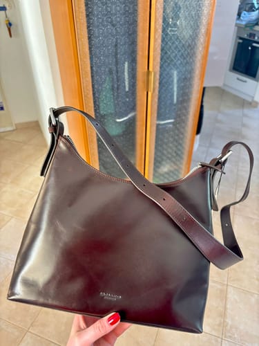 לקוחה מחזיקה את תיק הצד החום מעור של Vagabond Bari.