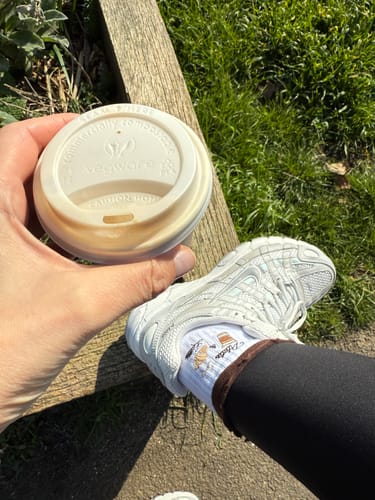 Customer relaxing outdoors wearing cute Pilates & Lattes socks with sneakers while holding a coffee.