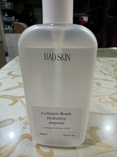 Customer's large, translucent bottle of Bad Skin Collagen Bomb Hydrating Ampoule on a table.