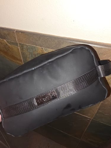 Reviewer holding their black Toiletry Bag, showing its material and useful side handle.