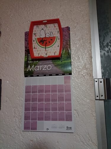 Reseñador muestra su reloj de pared Snoopy, de forma rectangular con marco rojo y diseño de sandía.