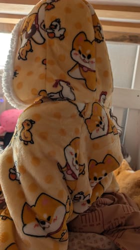 Reviewer from behind wearing the yellow wearable blanket, showing the soft hood and Shiba Inu pattern.