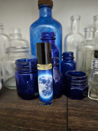 Customer's Blue Moon rollerball with a glowing moon label, placed among various blue and clear glass bottles.