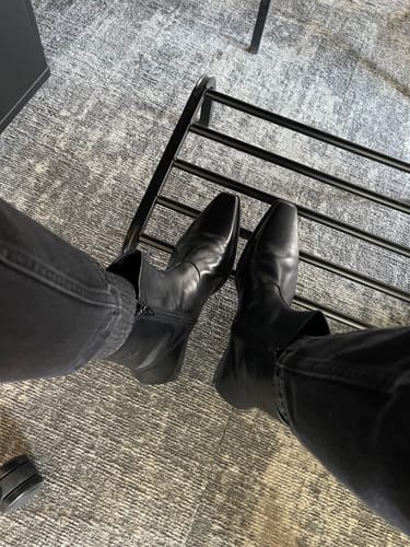 לקוחה מציגה מבט-על של מגפי Vagabond Nella שחורים מעור, עם חרטום מרובע.