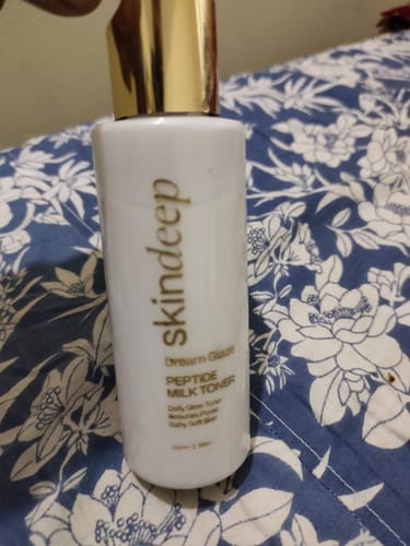 Customer holds the white Dream Glaze Peptide Milk Toner bottle with a gold cap against a floral background.
