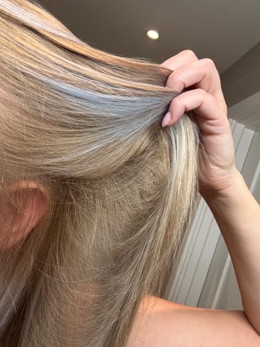 Customer lifts their blonde hair, revealing unwanted gray tones on the lengths after using Blonda Toning Shampoo.