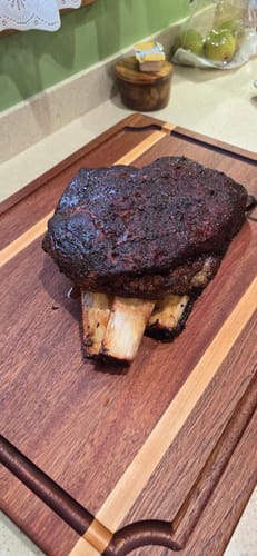 Customer's cooked Bone-In Short Ribs with a dark bark resting on a wooden cutting board.