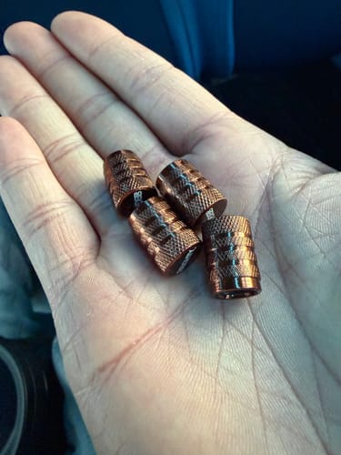 Reviewer holding four shiny, textured Bronze Valve Stem Caps in their open palm, showing the color.