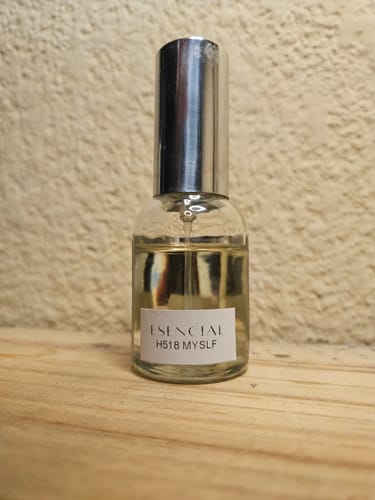 Cliente muestra el frasco de perfume H518 MYSLF con tapa plateada sobre una superficie de madera.