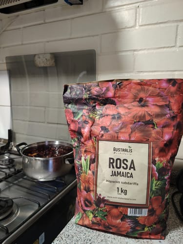 Reseñador mostrando una bolsa de Rosa Jamaica junto a una olla de infusión roja sobre la cocina.
