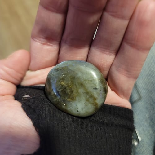 Customer holding a smooth, polished labradorite crystal from their subscription in their palm.