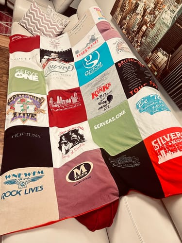 Customer's custom Project Repat T-Shirt Quilt with colorful patches draped over the side of a white sofa.