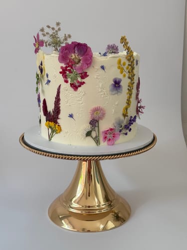 Customer's beautiful cake on a gold stand, decorated with colorful edible flowers from the Bespoke Bloomish Box.