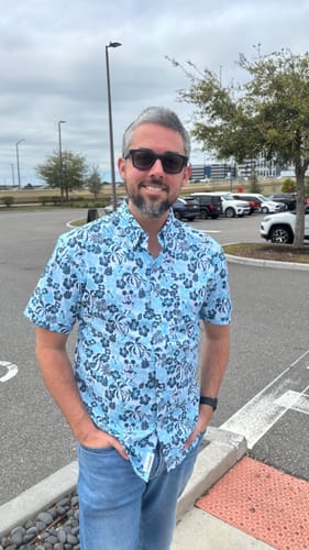 Reviewer standing outdoors wearing the blue patterned Disney "Aloha Pal" KUNUFLEX Short Sleeve Shirt.