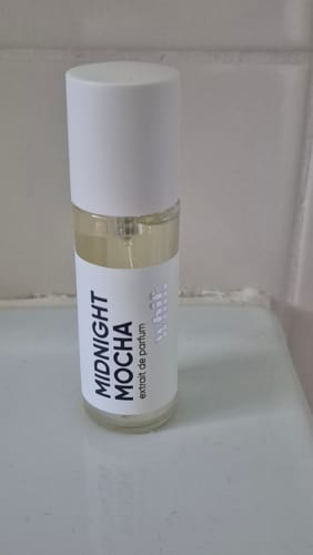 Customer's Midnight Mocha perfume in a clear glass bottle with a white label and cap, placed on a bathroom counter.