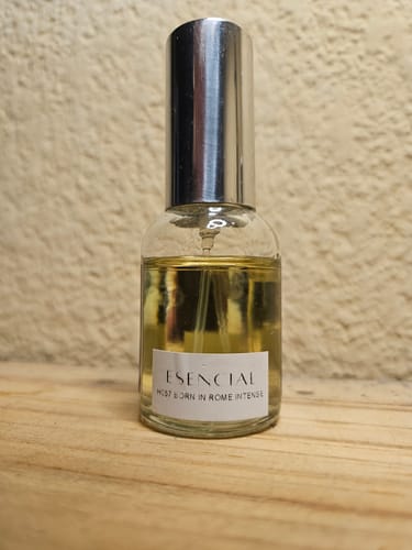 Foto de cliente del perfume H057 Born In Roma Intense en un frasco de vidrio con tapa plateada, sobre una superficie de madera.