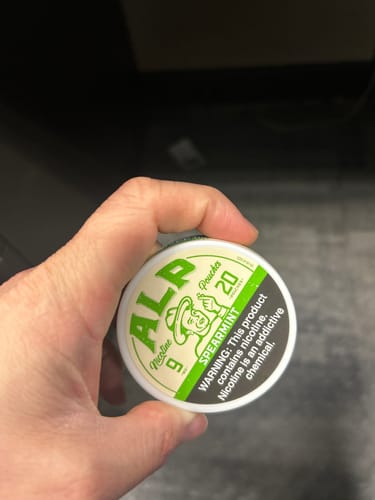Customer holding a white tin of ALP Spearmint Nicotine Pouches in their hand.