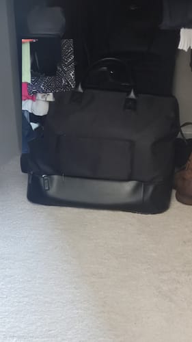 Customer's black Weekender Bag sitting on a carpet, showing its large size and bottom zip compartment.
