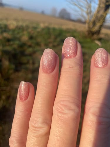 Nahaufnahme der Hand einer Kundin mit den funkelnden Rosé CatEye UV-Gel-Folien im Freien.