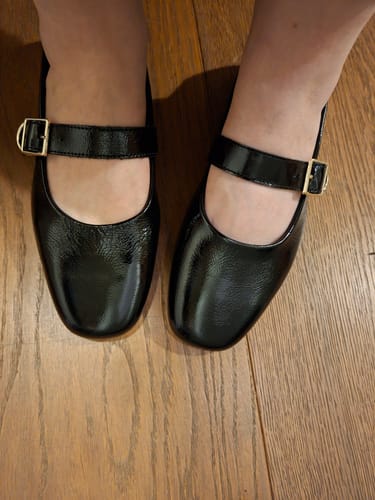 לקוחה מציגה את נעלי הבובה Jolin השחורות והמבריקות על רגליה.