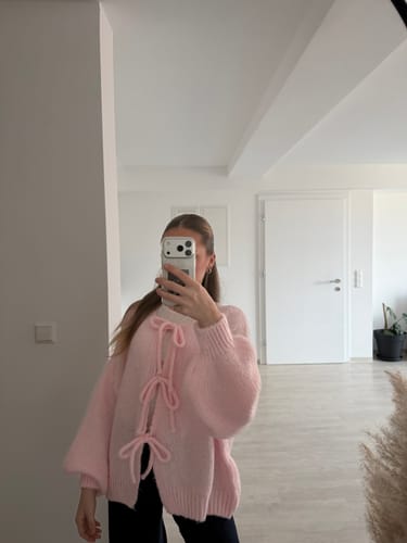 Kundin trägt das Überraschungsgeschenk, eine flauschige rosa Strickjacke mit Schleifen.