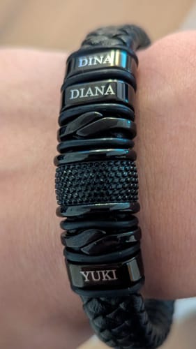 Close-up of a customer's personalized black bracelet on their wrist, engraved with the names Dina, Diana, and Yuki.