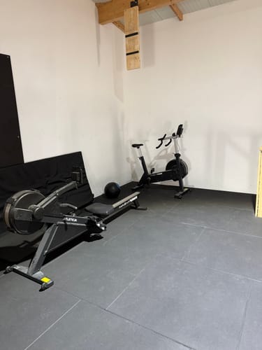 Ein Kunde zeigt das MagnaRev Ergometer in seinem Heim-Fitnessstudio neben einem Rudergerät.