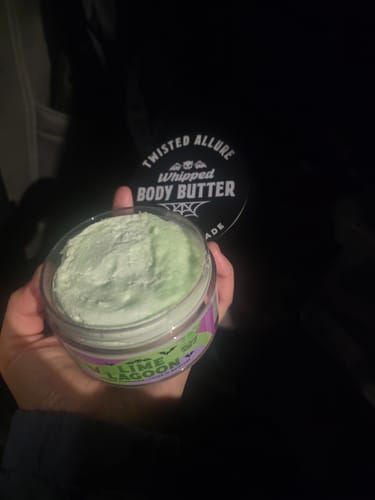Customer's hand holding an open jar of the light green, whipped Lime Lagoon Body Butter.