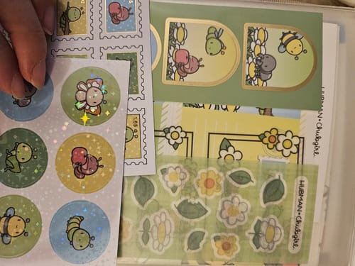Customer holding up 'Cute Critters' sticker sheets from their subscription, showing holographic and gold foil finishes.