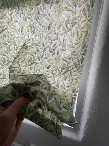 Customer holds a piece of Verdant Harmony fabric, with a finished blind made from it in the background.