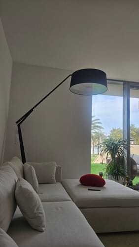 Customer's black Jumbo Retro Floor Lamp with an adjustable arm positioned over a light-colored sofa in a living room.