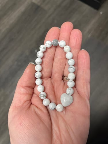 Customer holding the beaded white crystal bracelet with a heart charm in their open palm.