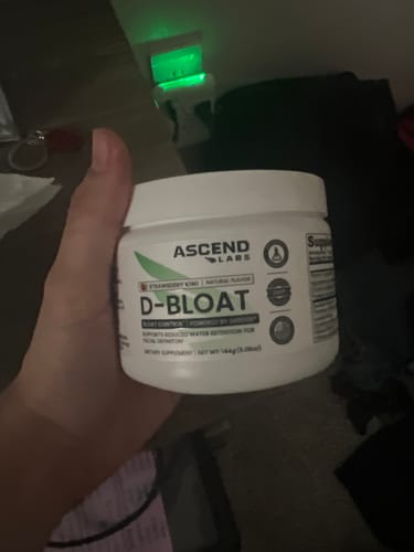 Customer's hand holding a white tub of D-BLOAT.