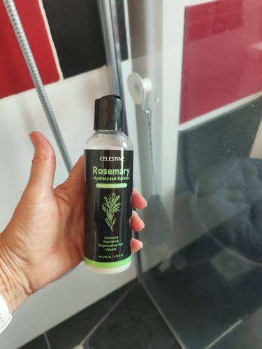 Customer holding a bottle of the organic rosemary and keratin shampoo in a shower.
