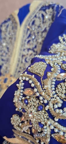 Close-up: Customer's Exclusive Lebsa Munia kaftan showing intricate gold embroidery and beading on the sapphire blue sleeve.