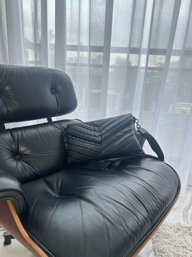 Reviewer's black, quilted Essential Clutch resting on a leather lounge chair.