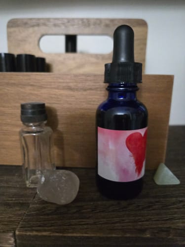 Customer's Love Dust Hair and Body Oil in its blue dropper bottle, sitting on a dark wooden surface next to a crystal.