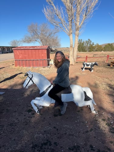 Customer posing on a horse statue while wearing the relaxed Avery Hoodie in Sedona Sage outdoors.