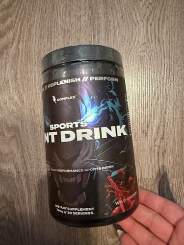 Reviewer holding a black tub of the Sports Iont Drink against a wooden surface.