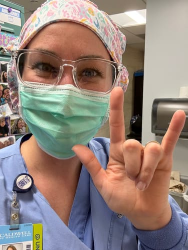 Reviewer in scrubs wearing the colorful DuoStyle Scrub Hat while making an 'I love you' hand sign.
