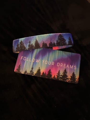Customer's Follow Your Dreams Bracelet with its colorful aurora design, displayed on a dark surface with its matching card.