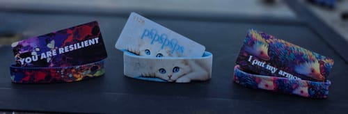 Customer's three colorful wristbands from a mystery pack, showing a cat, a hedgehog, and the phrase 'YOU ARE RESILIENT'.