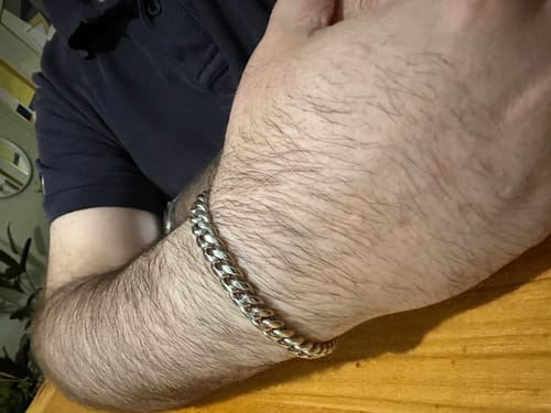 Cliente mostrando la pulsera Cuban de 8mm en su muñeca mientras descansa el brazo en una mesa.