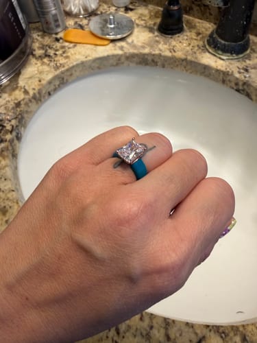 Customer wearing the Silicone Ring with a teal band and large emerald-cut stone over a sink.
